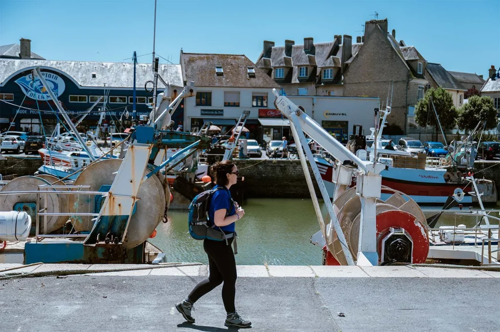 Femme avec un sac à dos marchant le long du port, à Port-en-Bessin-Huppain